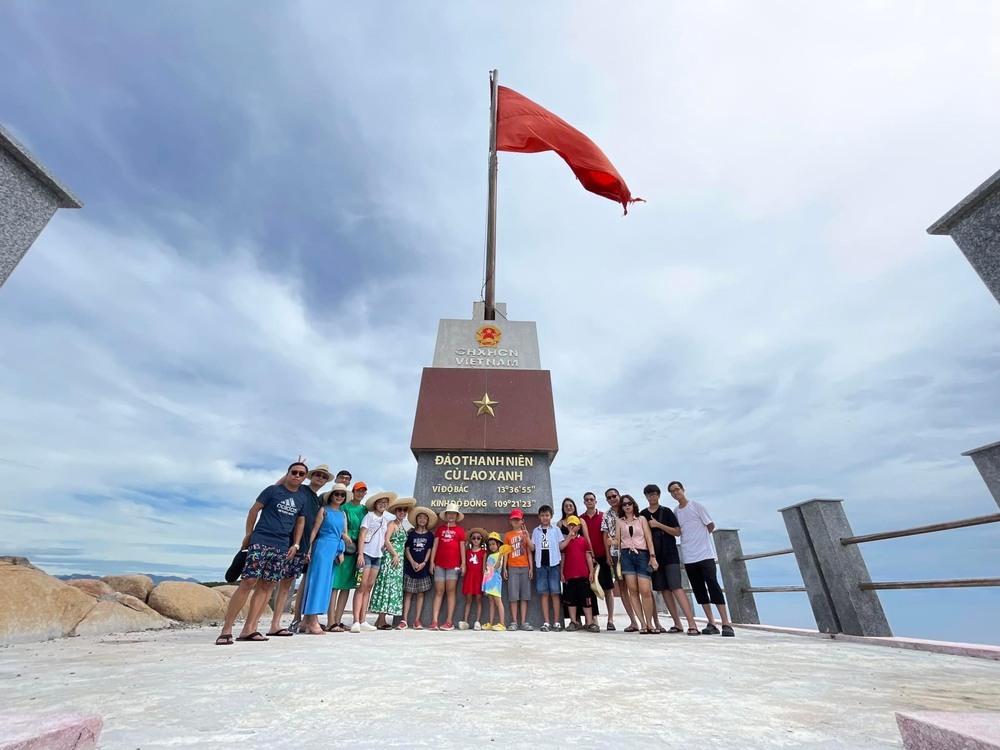 Du khách chụp ảnh lưu niệm dưới cột cờ thanh niên trên Cù Lao Xanh, với lá cờ Tổ quốc tung bay trong gió (Ảnh: Sưu tầm Internet)