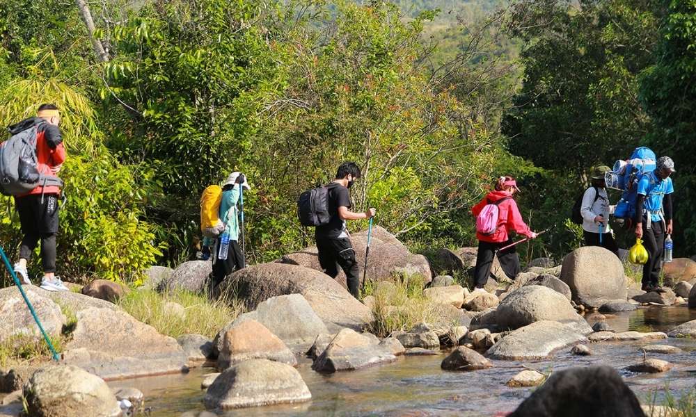 Du khách trekking qua con suối trong rừng Chư Yang Sin